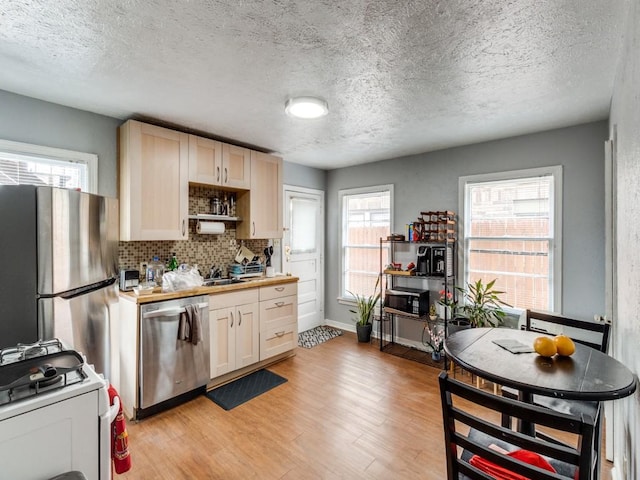 kitchen featuring light wood finished floors, backsplash, stainless steel appliances, light countertops, and baseboards