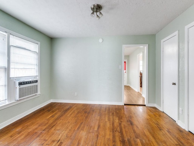 empty room with cooling unit, a textured ceiling, baseboards, and wood finished floors