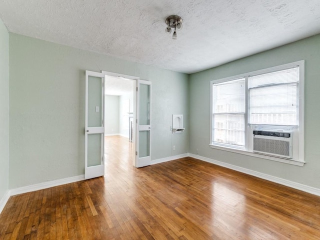 empty room featuring baseboards, wood-type flooring, a textured ceiling, and cooling unit