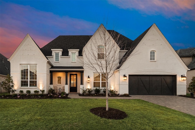 french country style house with brick siding, an attached garage, decorative driveway, and a front lawn