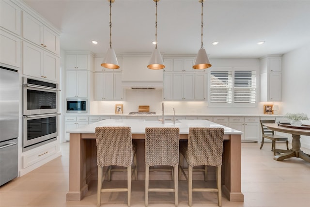 kitchen featuring a kitchen bar, light countertops, a center island with sink, and built in appliances