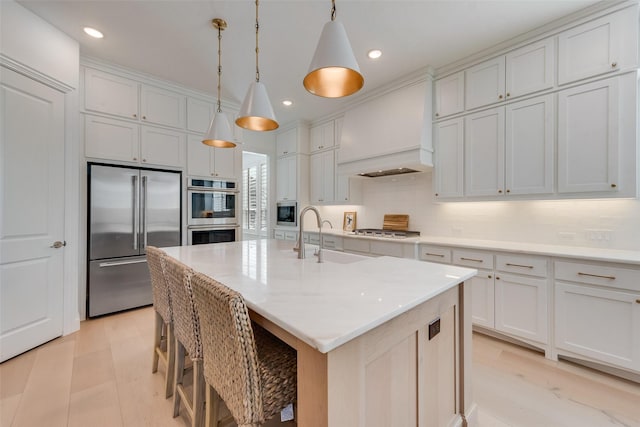 kitchen featuring premium range hood, built in appliances, an island with sink, recessed lighting, and a sink