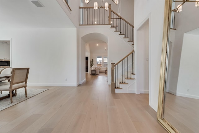 entryway with visible vents, a chandelier, stairs, light wood-style floors, and arched walkways