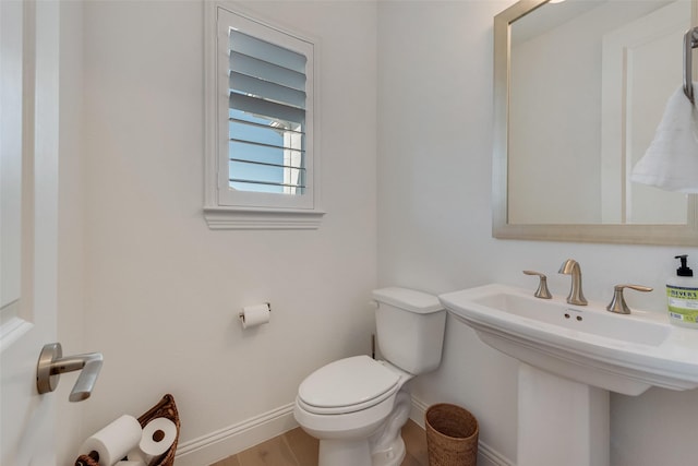 half bath with a sink, baseboards, toilet, and wood finished floors