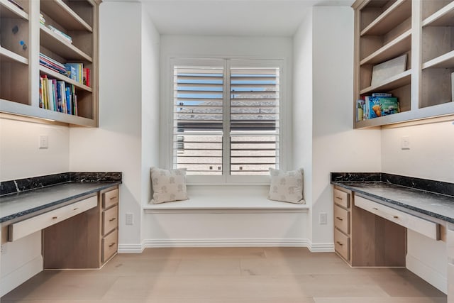 unfurnished office featuring baseboards, light wood-style floors, and built in desk