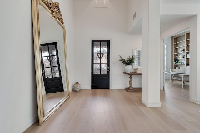 foyer featuring light wood finished floors, visible vents, baseboards, and a towering ceiling