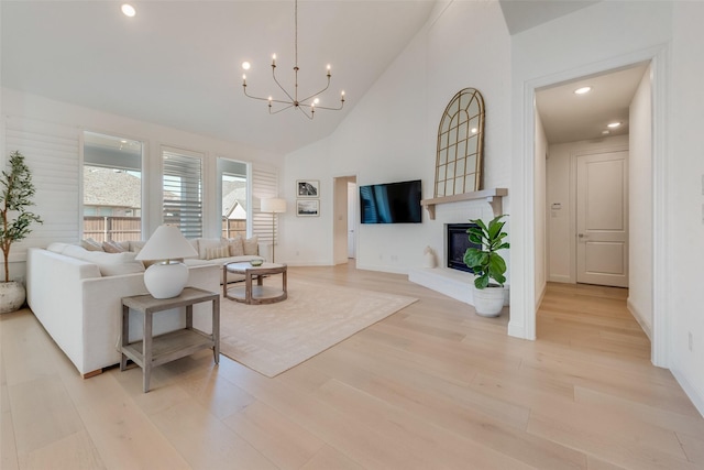 living area featuring high vaulted ceiling, a glass covered fireplace, recessed lighting, light wood-style floors, and an inviting chandelier