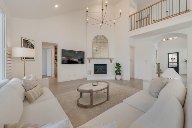 living area with arched walkways, an inviting chandelier, wood finished floors, and a towering ceiling