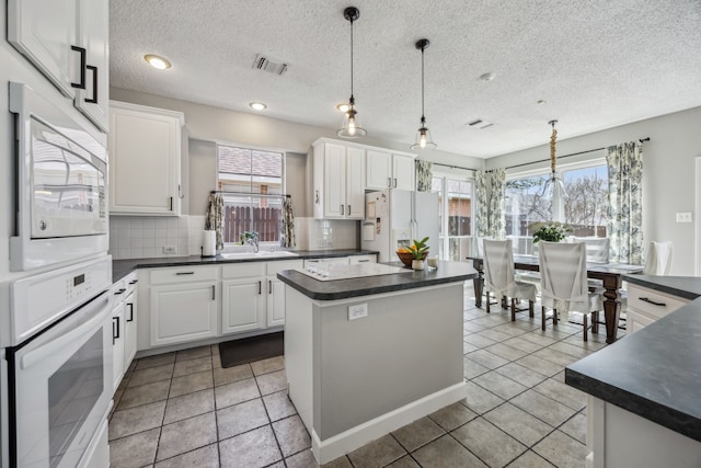 kitchen with white appliances, visible vents, dark countertops, tasteful backsplash, and a center island