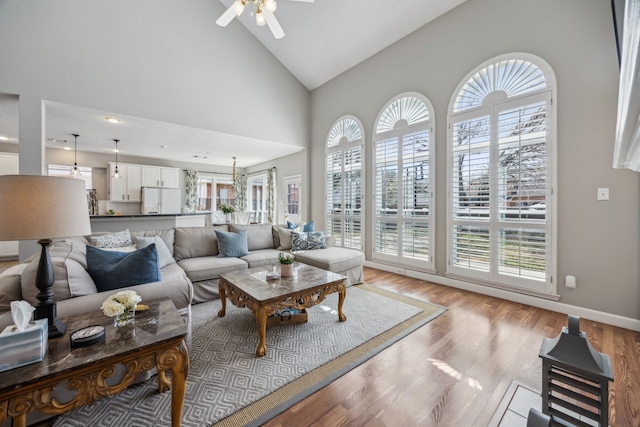 living area featuring high vaulted ceiling, baseboards, light wood-style floors, and a ceiling fan