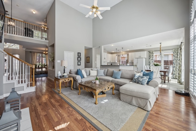 living room featuring wood finished floors, stairs, and ceiling fan with notable chandelier