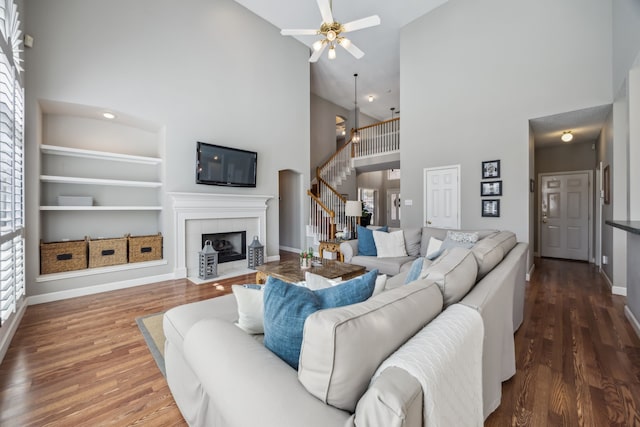 living area featuring baseboards, stairway, built in features, wood finished floors, and a ceiling fan