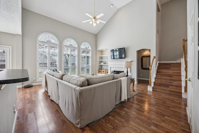 living area featuring baseboards, dark wood finished floors, stairway, a fireplace, and a ceiling fan