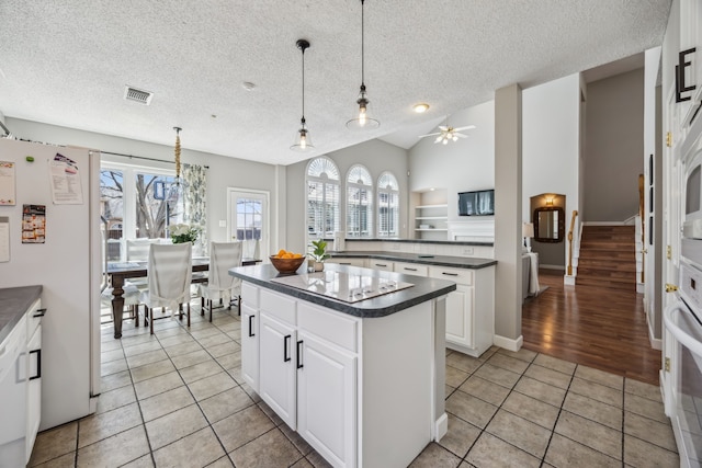 kitchen featuring white appliances, light tile patterned floors, visible vents, a kitchen island, and dark countertops