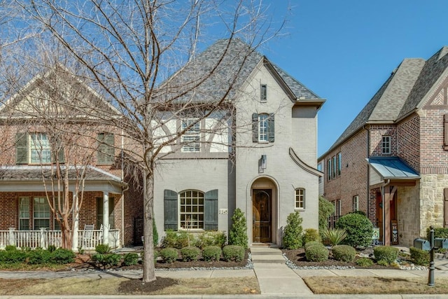 french country inspired facade featuring a porch and brick siding