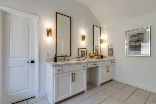 bathroom featuring double vanity, baseboards, lofted ceiling, and a sink