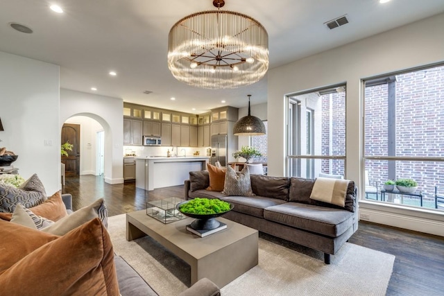 living room with visible vents, recessed lighting, an inviting chandelier, arched walkways, and dark wood-style flooring