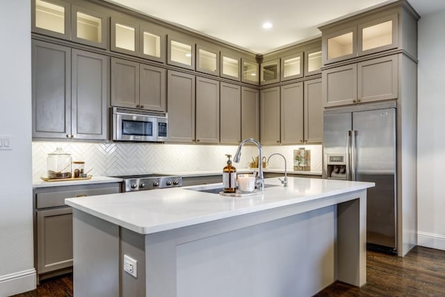 kitchen featuring a center island with sink, a sink, light countertops, appliances with stainless steel finishes, and tasteful backsplash