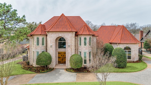 view of front facade with brick siding, a tiled roof, and a front yard