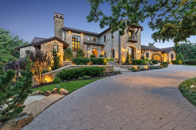 mediterranean / spanish home featuring a balcony, a chimney, stone siding, and curved driveway