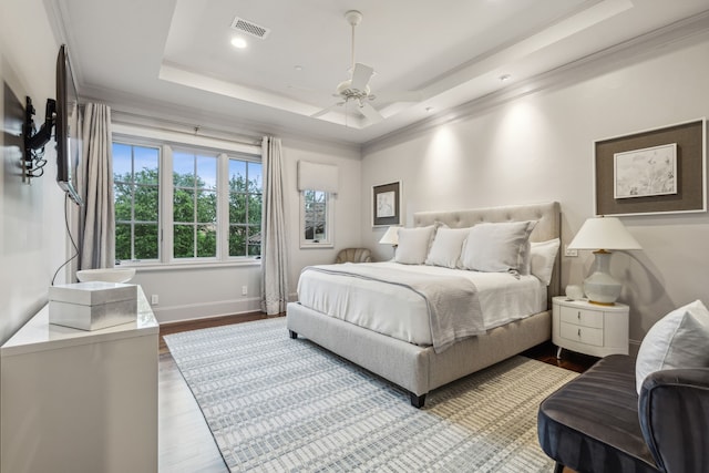 bedroom featuring visible vents, baseboards, ornamental molding, wood finished floors, and a raised ceiling