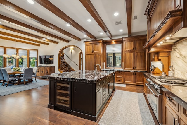 kitchen with a kitchen island with sink, dark stone countertops, arched walkways, wine cooler, and range with two ovens