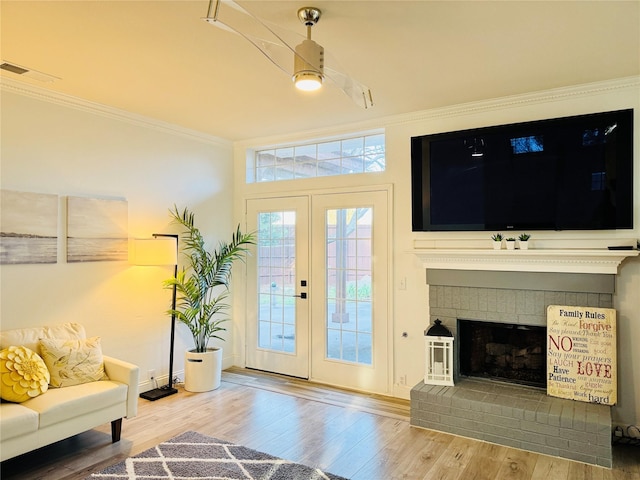 living area featuring visible vents, wood finished floors, a brick fireplace, and ornamental molding