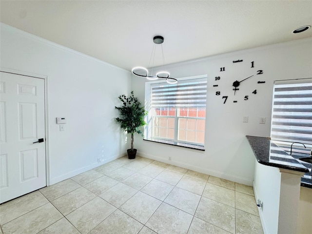 unfurnished dining area with light tile patterned floors, a chandelier, crown molding, and baseboards