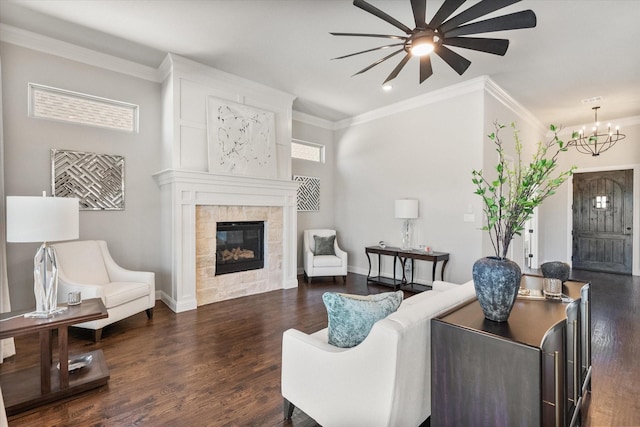 living room featuring plenty of natural light, dark wood-style flooring, a tiled fireplace, crown molding, and ceiling fan with notable chandelier