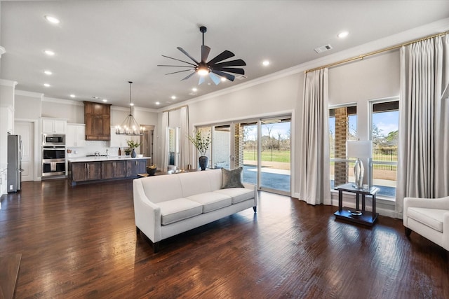 living area featuring visible vents, recessed lighting, dark wood-type flooring, crown molding, and ceiling fan with notable chandelier