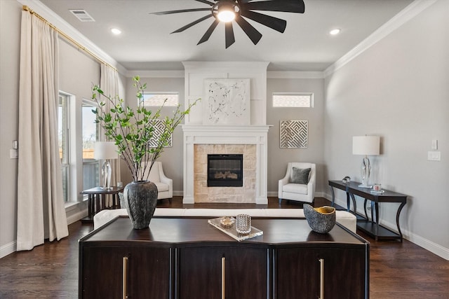 living room featuring a tiled fireplace, dark wood-type flooring, a ceiling fan, and ornamental molding