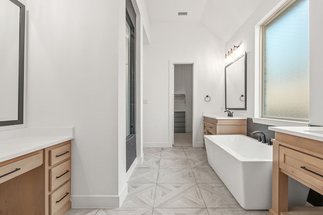 full bathroom featuring visible vents, two vanities, a sink, a freestanding bath, and vaulted ceiling