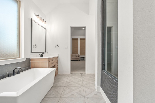 full bath featuring vanity, a soaking tub, baseboards, and lofted ceiling