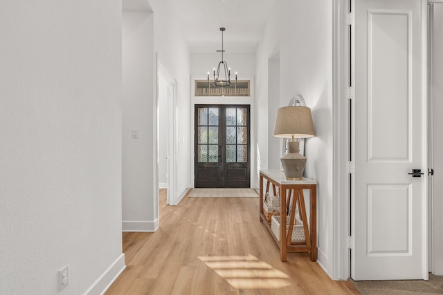 foyer entrance with light wood-style floors, baseboards, french doors, and a chandelier