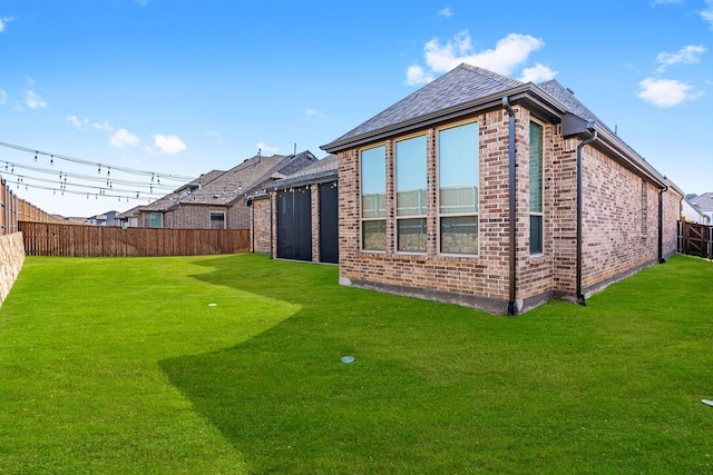 rear view of property featuring brick siding, a fenced backyard, and a lawn