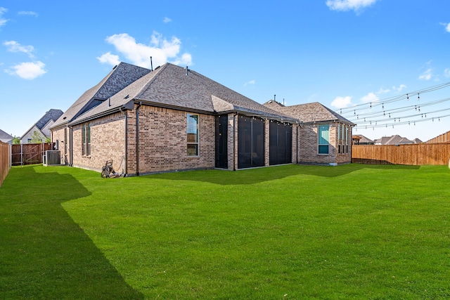 back of property with a yard, brick siding, central AC unit, and a fenced backyard