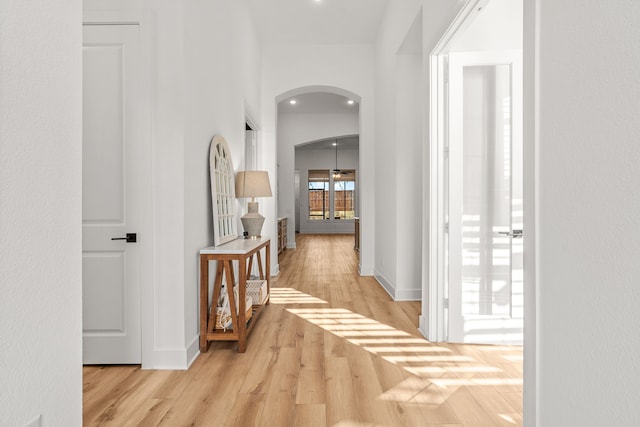 hallway with arched walkways, baseboards, and wood finished floors