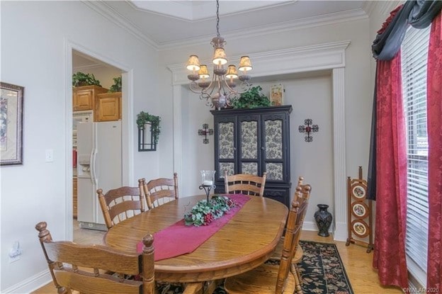 dining space with light wood-style flooring, a notable chandelier, baseboards, and ornamental molding