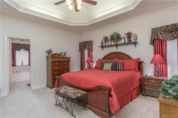 bedroom with ceiling fan, a tray ceiling, crown molding, and light carpet