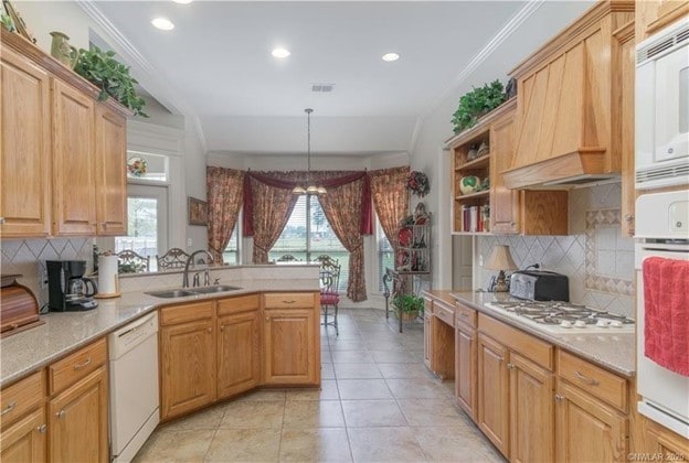 kitchen featuring white appliances, custom exhaust hood, a peninsula, ornamental molding, and a sink