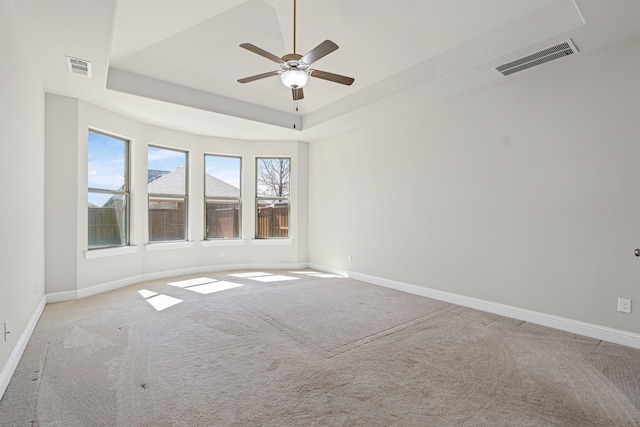 carpeted spare room featuring a tray ceiling, visible vents, baseboards, and ceiling fan