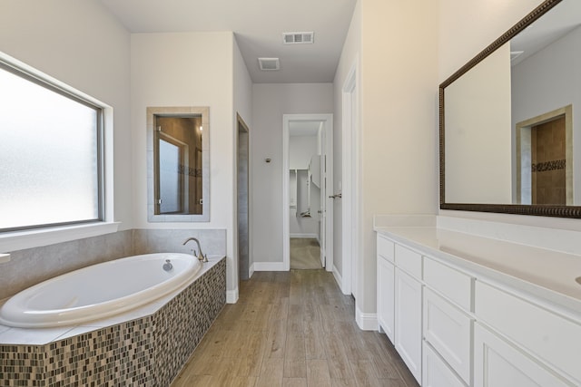 bathroom featuring visible vents, wood finished floors, a bath, and vanity