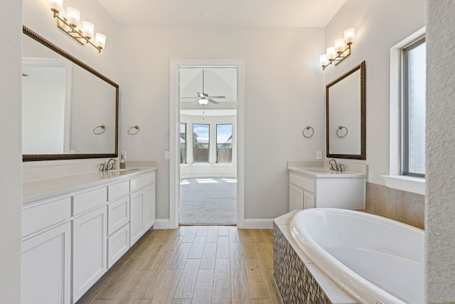 full bathroom featuring baseboards, a relaxing tiled tub, ceiling fan, wood finished floors, and vanity