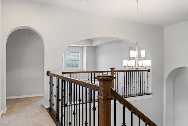 hall with baseboards, carpet, an inviting chandelier, and an upstairs landing