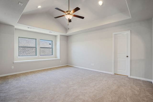 carpeted spare room featuring baseboards, visible vents, ceiling fan, vaulted ceiling, and a raised ceiling