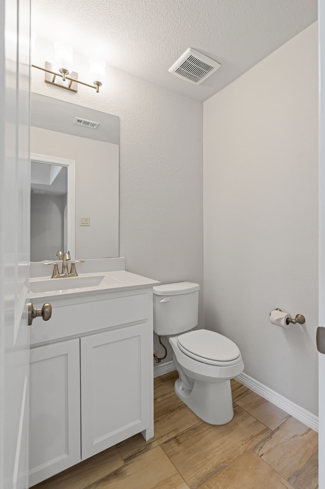 half bath featuring vanity, toilet, wood finished floors, and visible vents