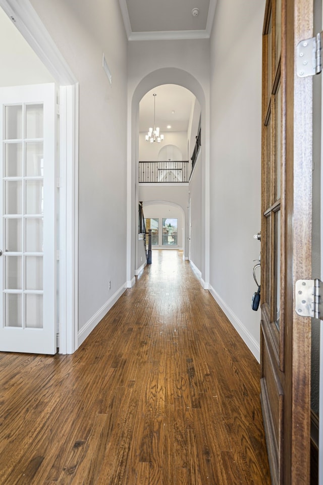 entrance foyer with dark wood-style floors, arched walkways, an inviting chandelier, crown molding, and baseboards