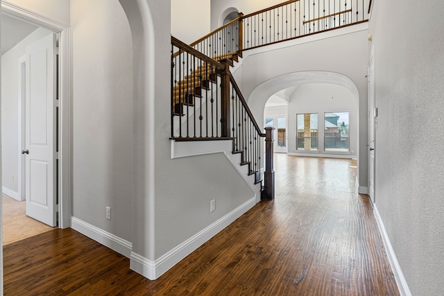 foyer entrance with arched walkways, baseboards, and wood-type flooring