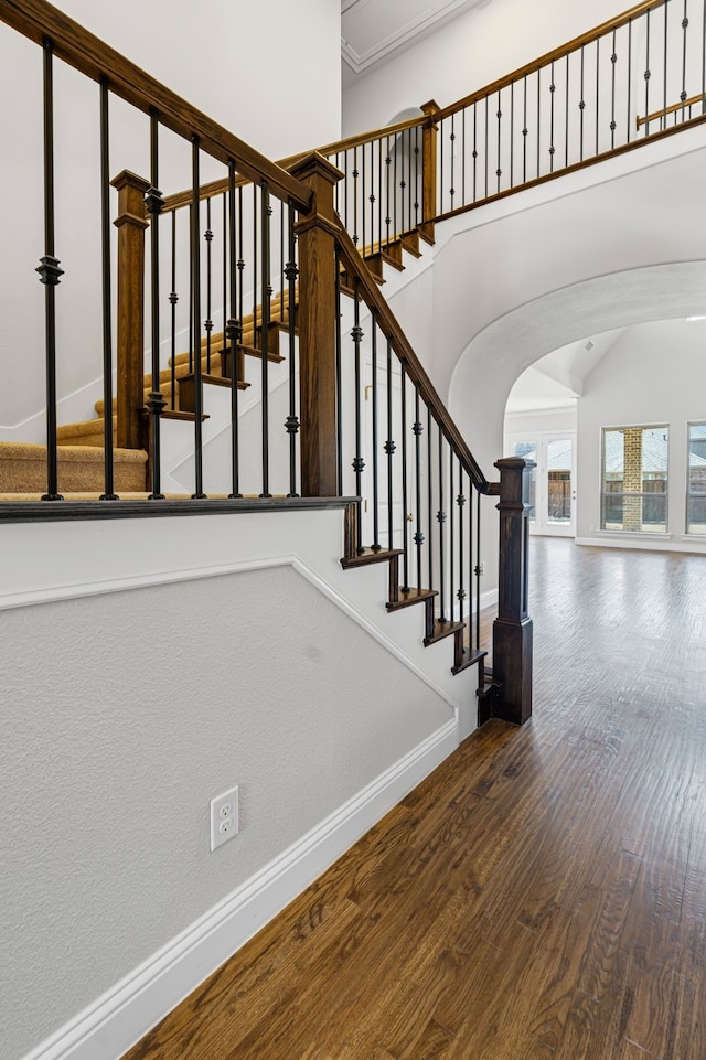 stairs with wood finished floors, arched walkways, a towering ceiling, and baseboards