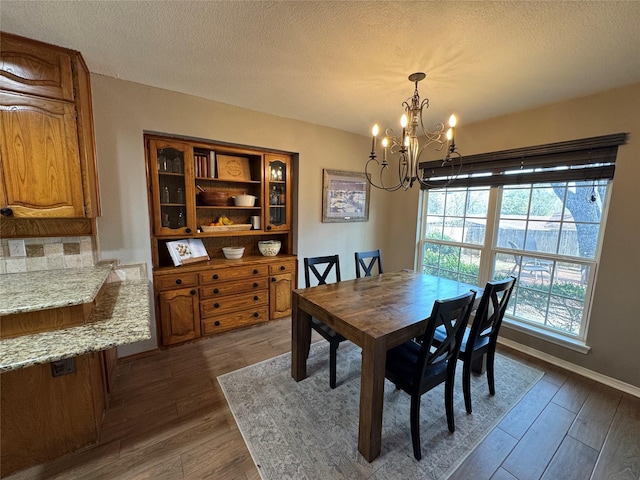 dining space featuring dark wood finished floors, a notable chandelier, baseboards, and a textured ceiling